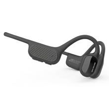 A photorealistic studio product photograph captures the OPN Sound Swym+ open-ear headphones in charcoal grey, angled to show the left side control panel and earpiece on a seamless pure white background with a soft shadow.