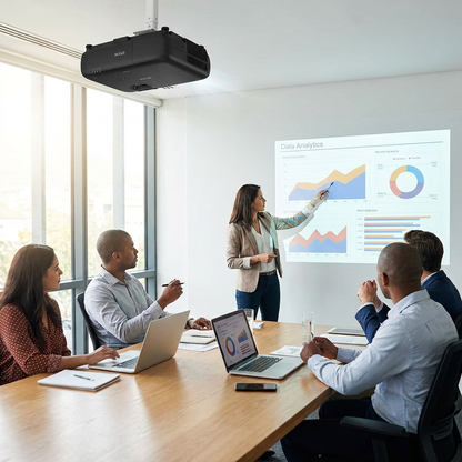 A photorealistic lifestyle scene shows the black Epson PowerLite L265F projector, ceiling-mounted in a bright, sunlit office meeting room. A team of professionals is engaged in a business presentation, with a woman pointing to data charts projected onto a large screen.