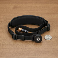 Black padded Canon Camera Strap E2 with a quarter-inch tripod-style screw mount, coiled on a wooden surface beside an AA battery and a coin for size reference.
