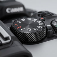 Close-up of the top mode dial on a black Canon EOS R50 camera, showing shooting-mode settings including M, Av, Tv, and SCN, with a textured knurled grip.