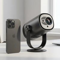 A scale photo of the dark gray Dangbei Freedo projector next to a smartphone on a white desk.
