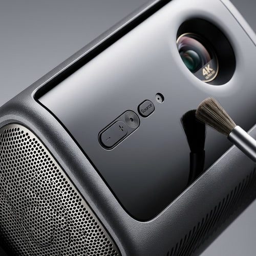 An extreme close-up photograph showcasing the complex multi-texture surface, the 4K Ultra HD lens detail, and the precise control buttons of the Dangbei MP1-Max projector.