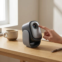 Dangbei N2 Mini projector on desk next to coffee mug and hand for scale.