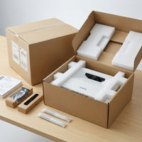 Epson BrightLink interactive projector unboxing: the white projector seated in foam inside its open box, with two interactive pens, cables, and a manual laid out alongside the shipping carton.