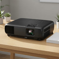Black Epson PowerLite projector on a wooden desk in an office, with potted succulents and a stack of paper nearby.