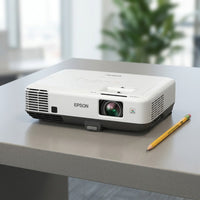 A photorealistic image of the Epson PowerLite 535W projector beside a standard pencil, in a well-lit office, showing its scale.