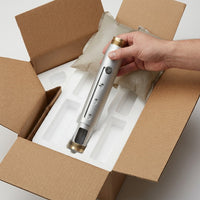 Hand lifting a silver Epson 9–12" adjustable projector extension column with brass threaded ends from its foam-lined shipping box.