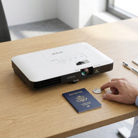 A photo of the projector seen on an office desk next to a passport and a coin to show its compact size.