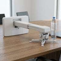 Scale reference view: the white ultra-short throw wall mount on a textured wooden conference desk.