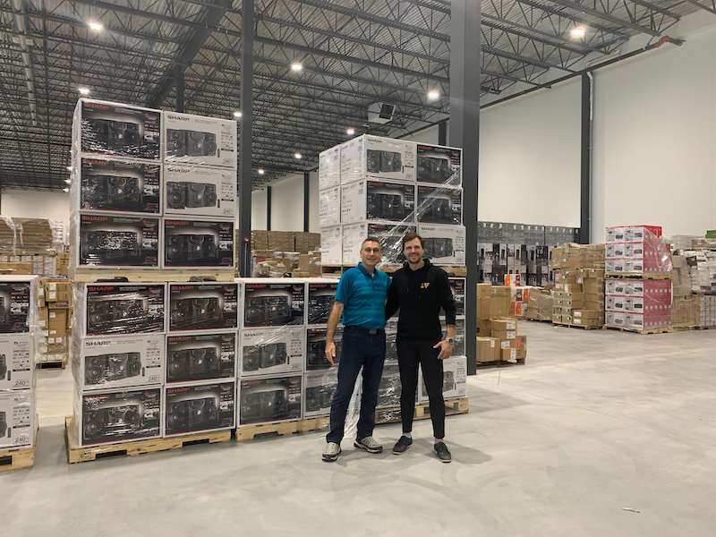 Two team members at the Montreal warehouse in front of Sharp Sound Systems stock