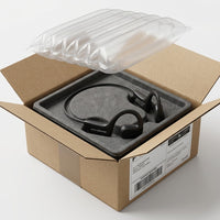 Black OPN Sound Aperto open-ear headphones resting in a molded grey insert inside an open Canada Post shipping box, with a clear inflatable air cushion on top.