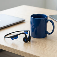 A scale-reference image of OPN Sound Mezzo+ bone conduction headphones beside a standard coffee mu