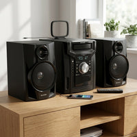 A 3/4 perspective lifestyle shot of the SHARP CD-BH950 stereo system with detached speakers, remote, and antennas on a contemporary oak credenza with natural window light.