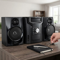 Black Sharp CD-BH950 shelf stereo system with CD player and two bookshelf speakers on a wood console in a bright living room, with a person reaching for keys beside a notebook and pen.