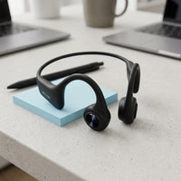 A realistic photo of a SHARP HP-BC55 matte black bone conduction earphones on a desk next to a pen and a standard stack of blue sticky notes for size comparison.