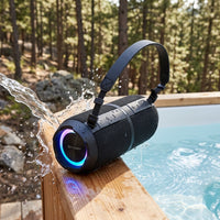 A waterproof Sharp speaker on a wooden dock with water splashing, RGB lights, in a natural forest setting.