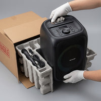 Sharp PS-914 portable Bluetooth party speaker being lifted from its moulded pulp packaging tray, with the included wired microphone and USB cable beside it