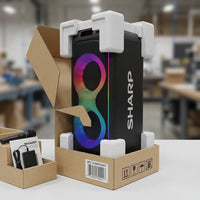 Black Sharp PS-935 party speaker with a colourful RGB-lit front panel, shown in its opened retail box with protective foam end-caps, alongside an included microphone, power adapter, and manual.