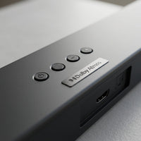 A macro view of the Sharp HT-SBW53121 soundbar, featuring detailed power, volume, and input buttons, along with visible HDMI and optical ports.